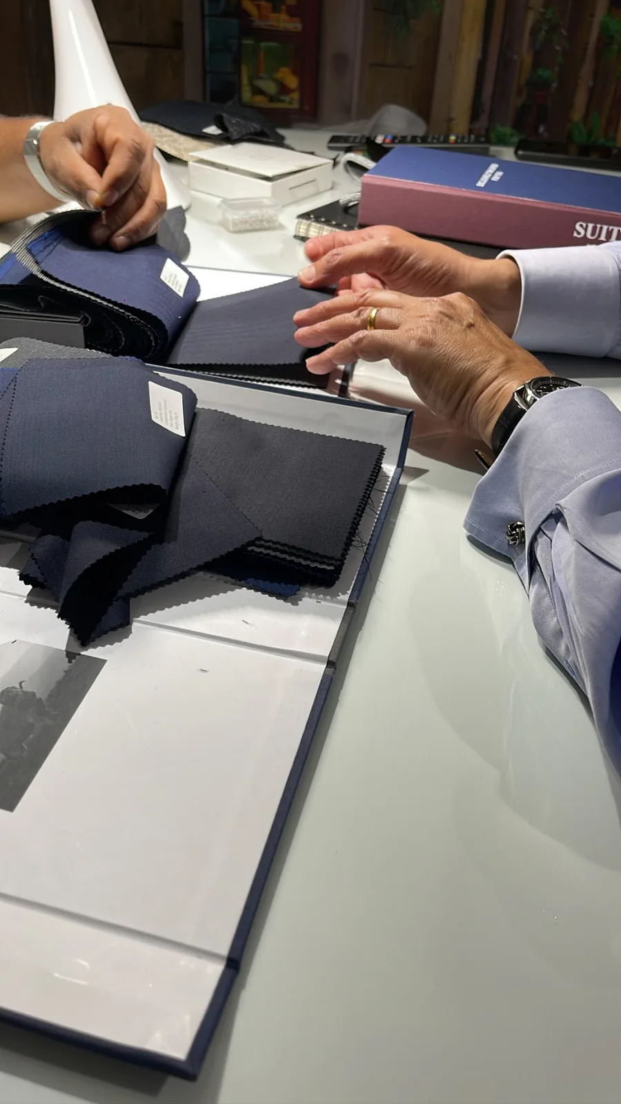 Hands turning the pages of a navy suiting book across the studio table while choosing fabric