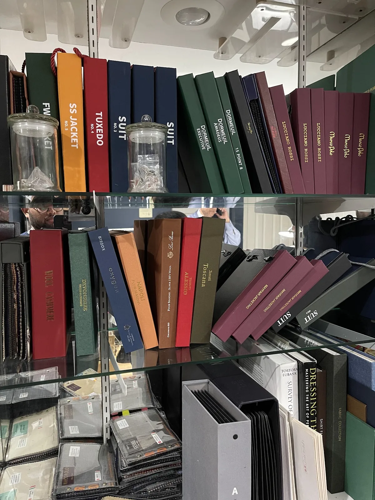 Shelves of fabric sample books at the studio, spines labelled Tuxedo, Suit, SS Jacket and Dressing