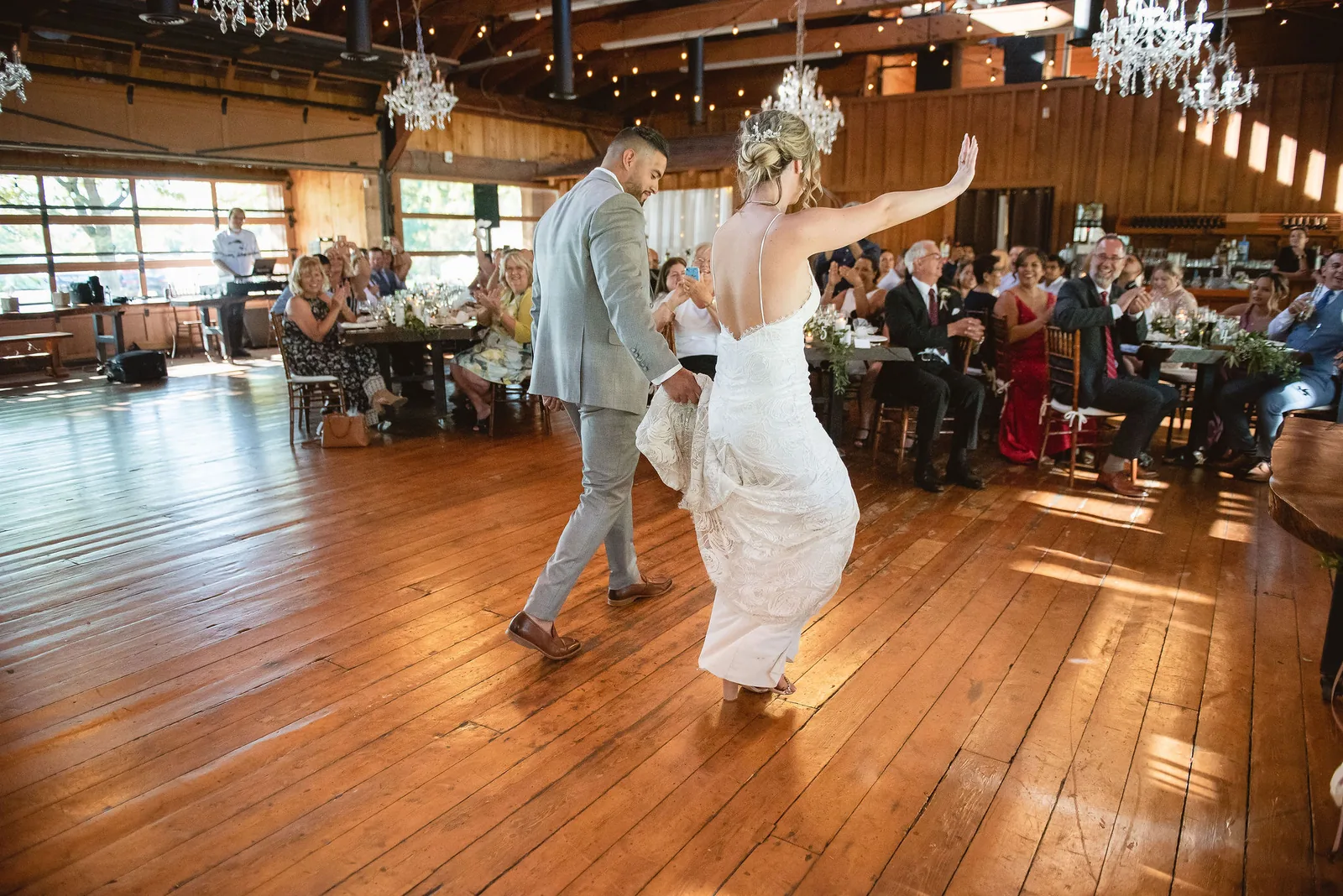 The first dance under chandeliers, the groom in a light grey suit turning his bride on a wooden floor