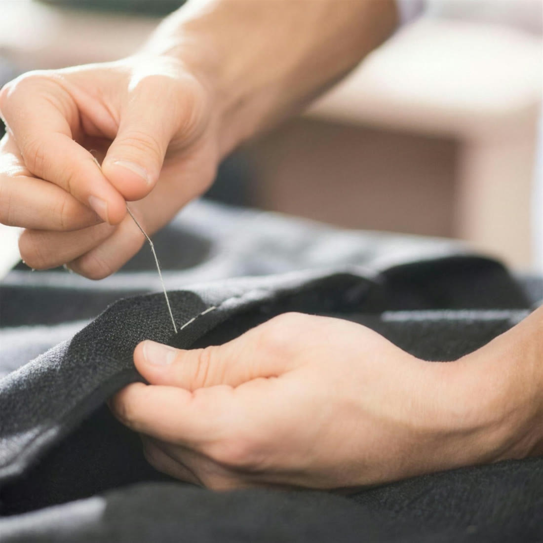 Sam at the tailoring bench, hand-stitching a garment