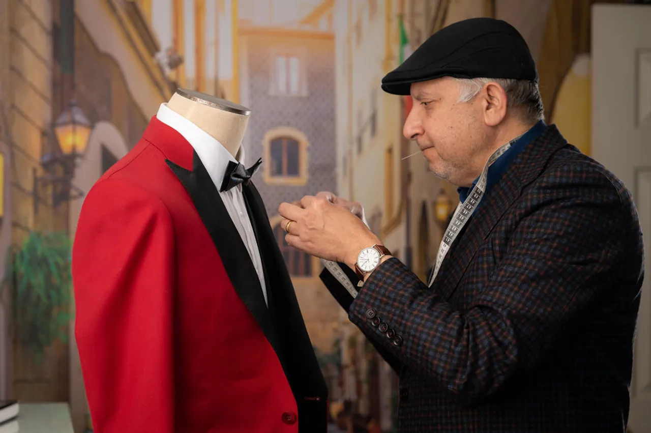 Sam pinning a red dinner jacket with a black shawl lapel on the dress form, tape around his neck